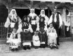 Család ünneplőben, faragott oszlopos tornác előtt (Kórógy, v. Szerém m., 1910)